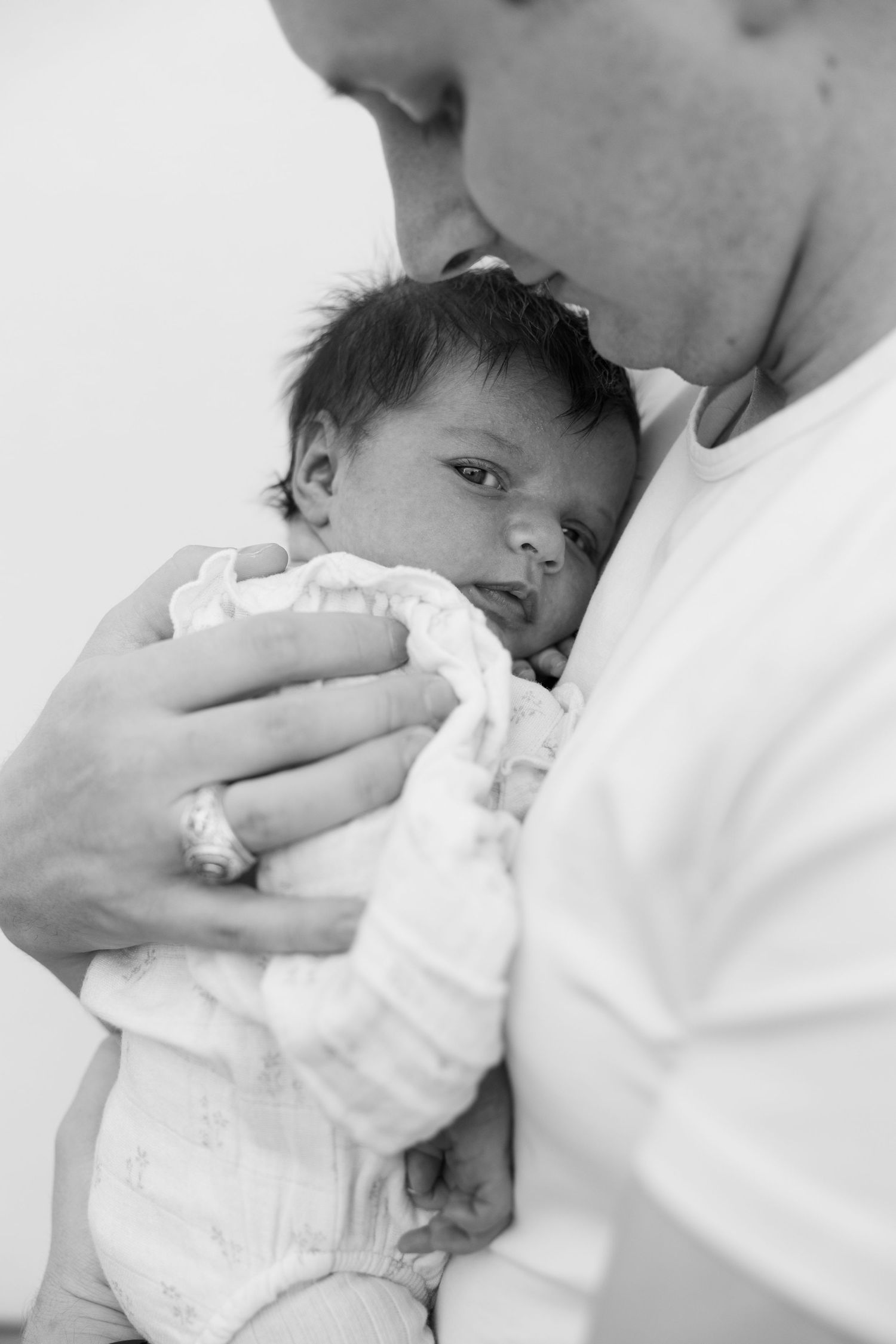 Black and white close-up of a father tenderly holding and gazing at his newborn baby wrapped in white.