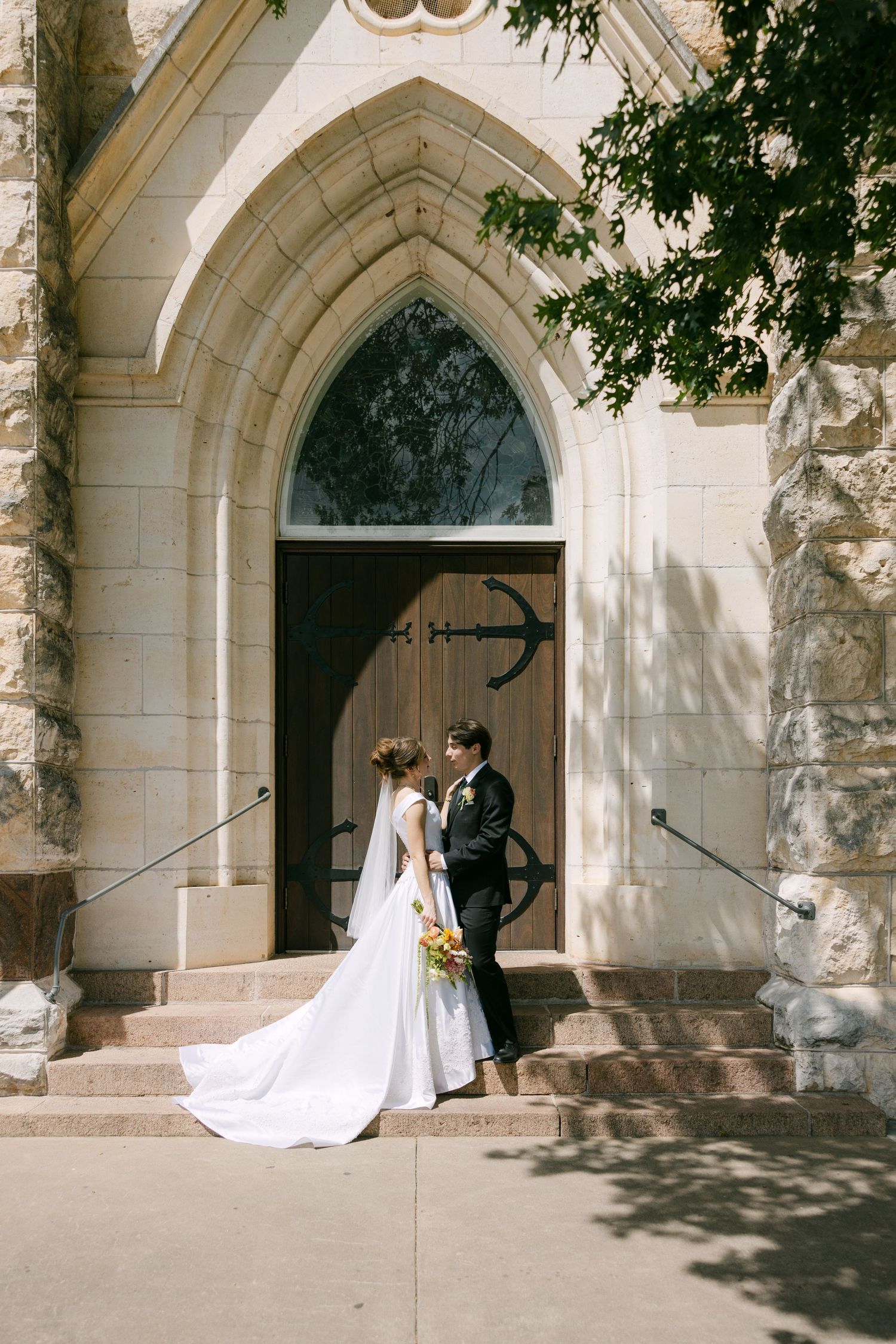 Bride and groom stand together at the entrance of a beautiful stone Gothic church on their wedding day.