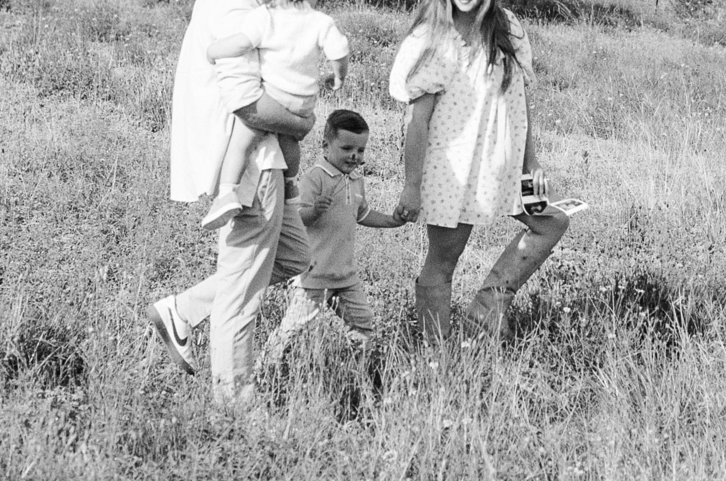 Black and white photo of a family walking through a grassy field together.