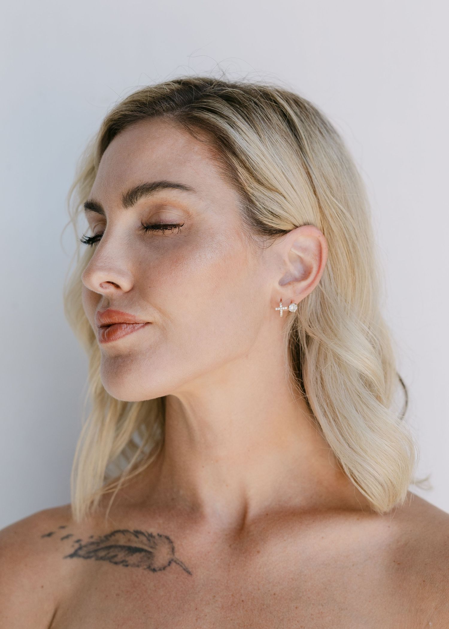 Close-up profile of blonde woman showcasing delicate cross earrings with eyes closed.