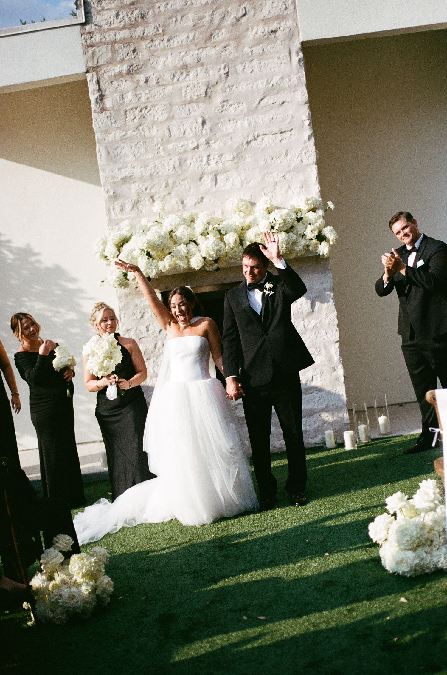 Joyful bride and groom celebrate at outdoor wedding ceremony with white floral arrangements.