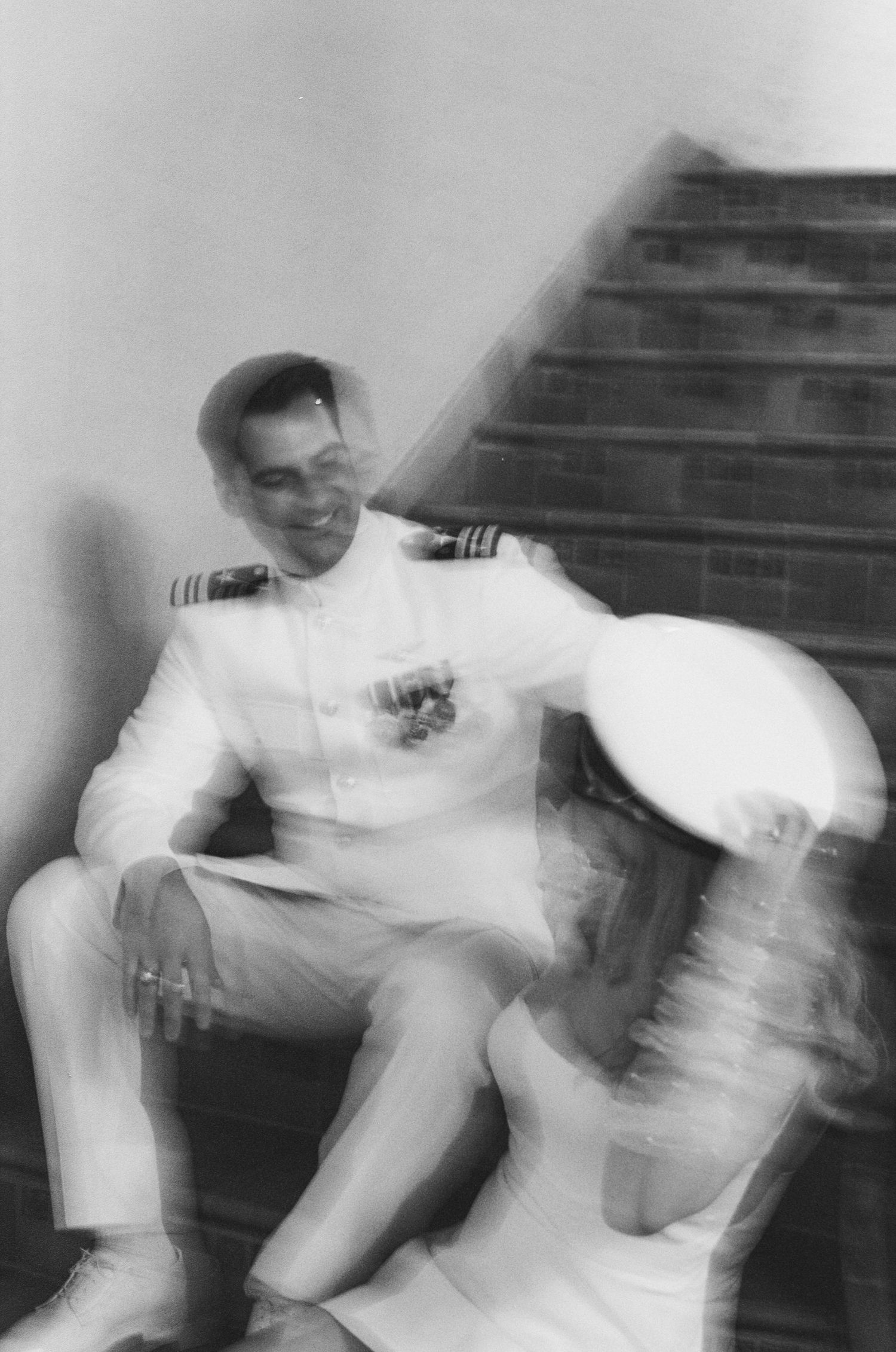 Artistic blurred black and white photo of military groom and bride sitting together on staircase steps.