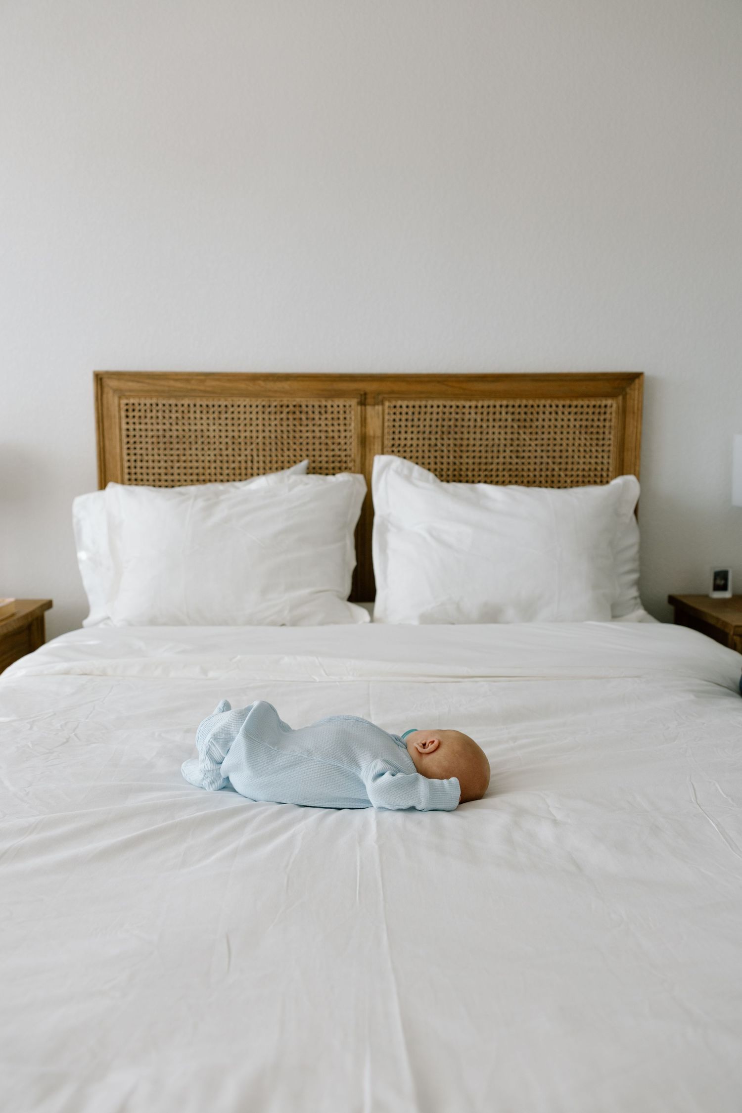 Newborn baby sleeping peacefully on a white bed in a light blue onesie.