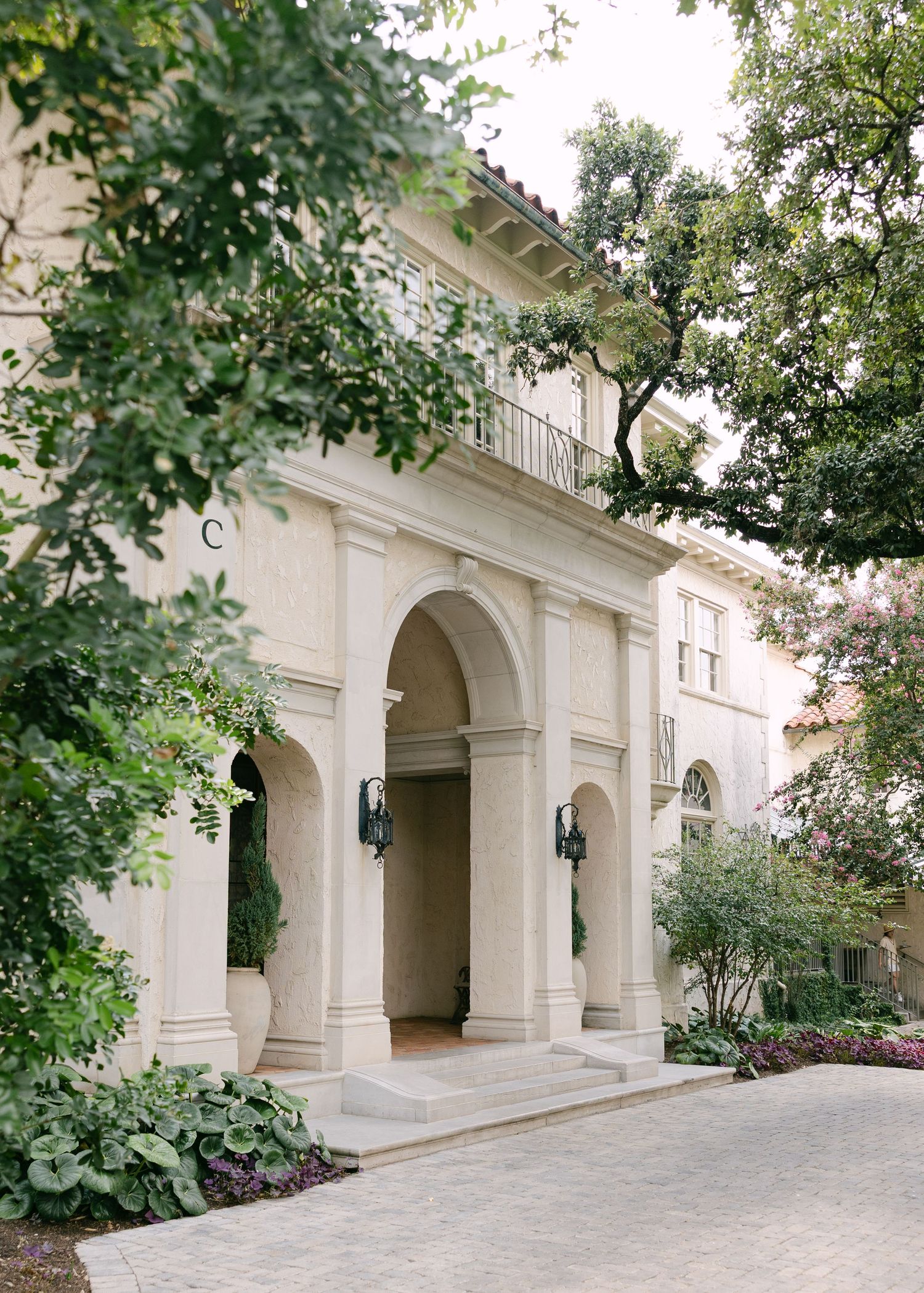 Grand Italian-style wedding venue exterior featuring arched entryway, stone columns, and lush garden landscaping.