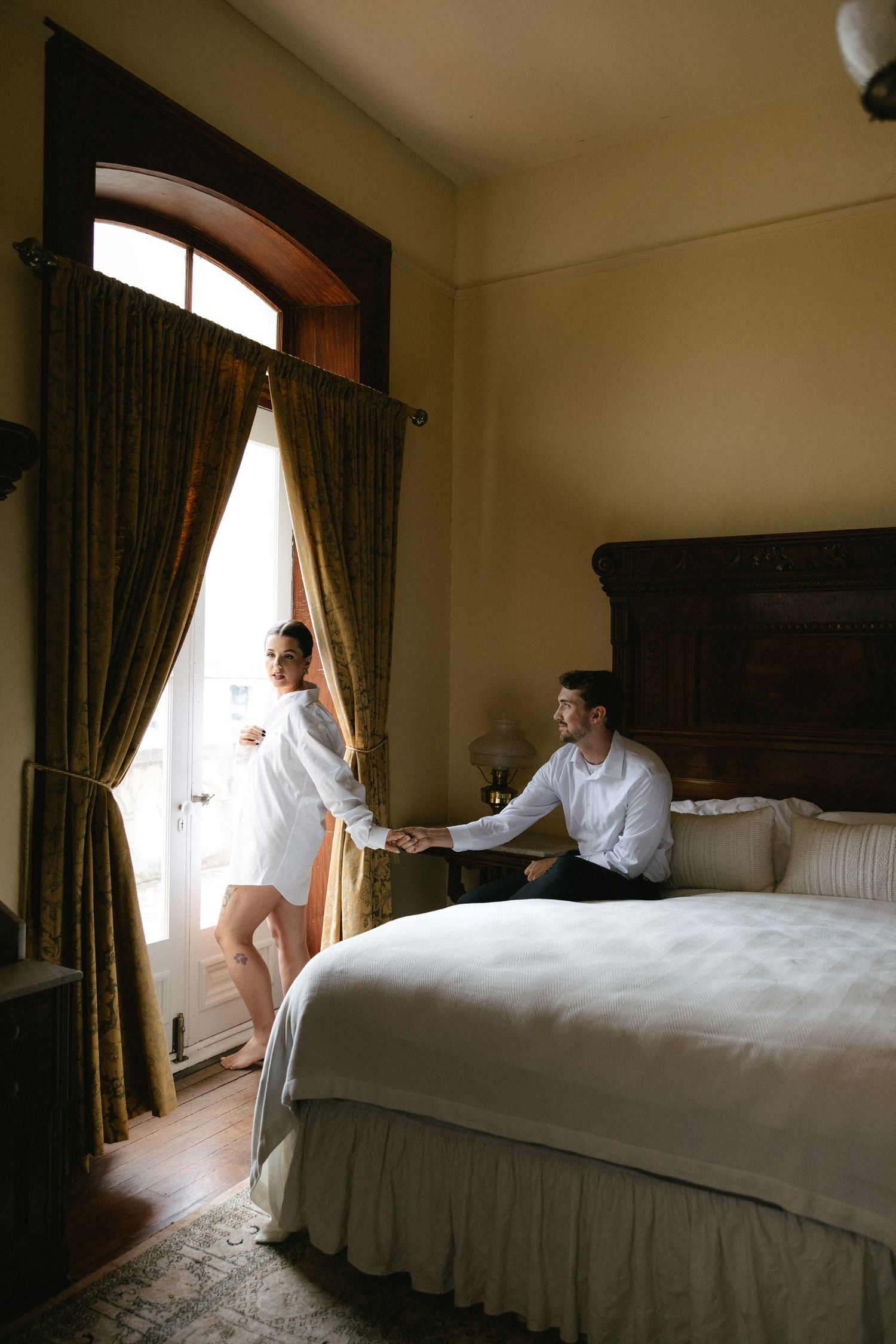 Couple holding hands in a warmly lit vintage hotel room on their wedding morning.