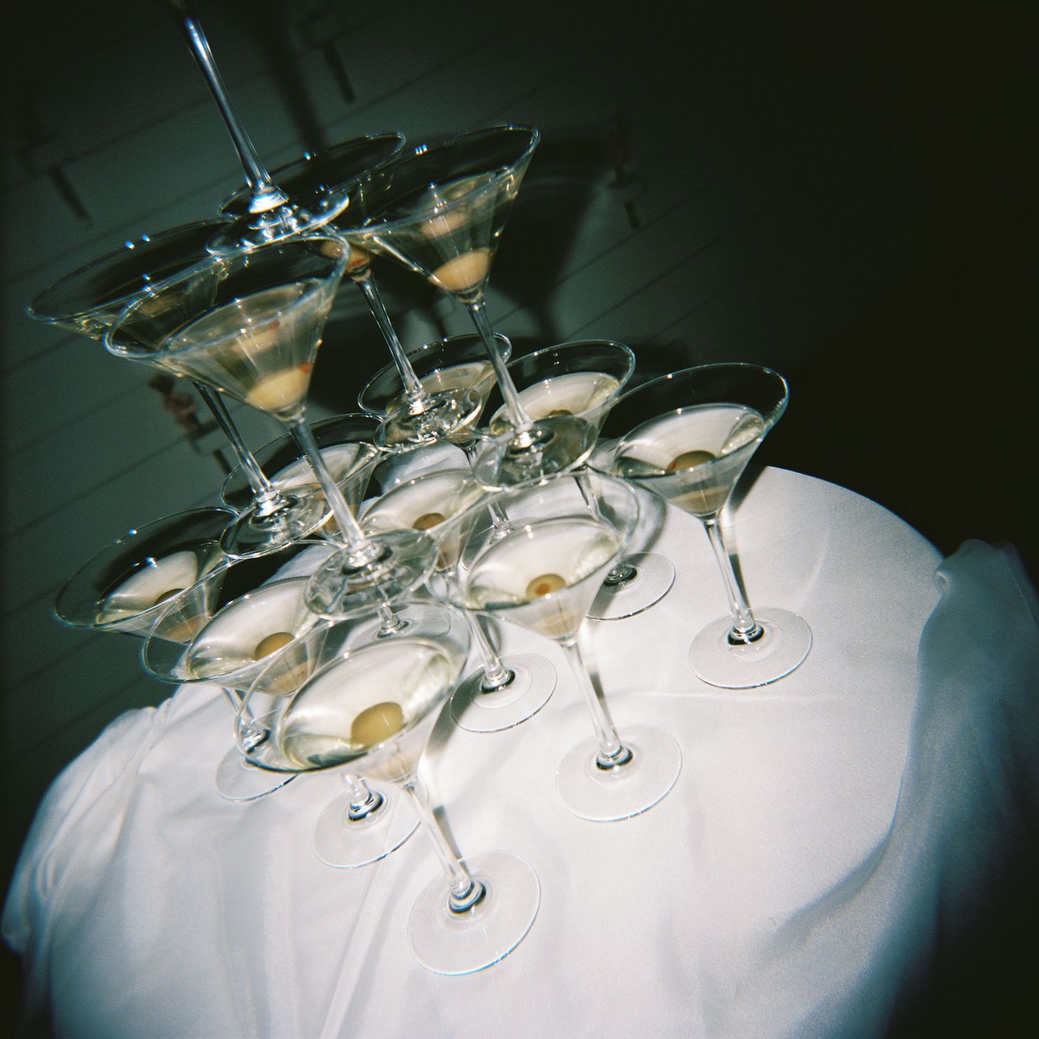 Pyramid of martini glasses with olives arranged on a white tablecloth at a wedding.