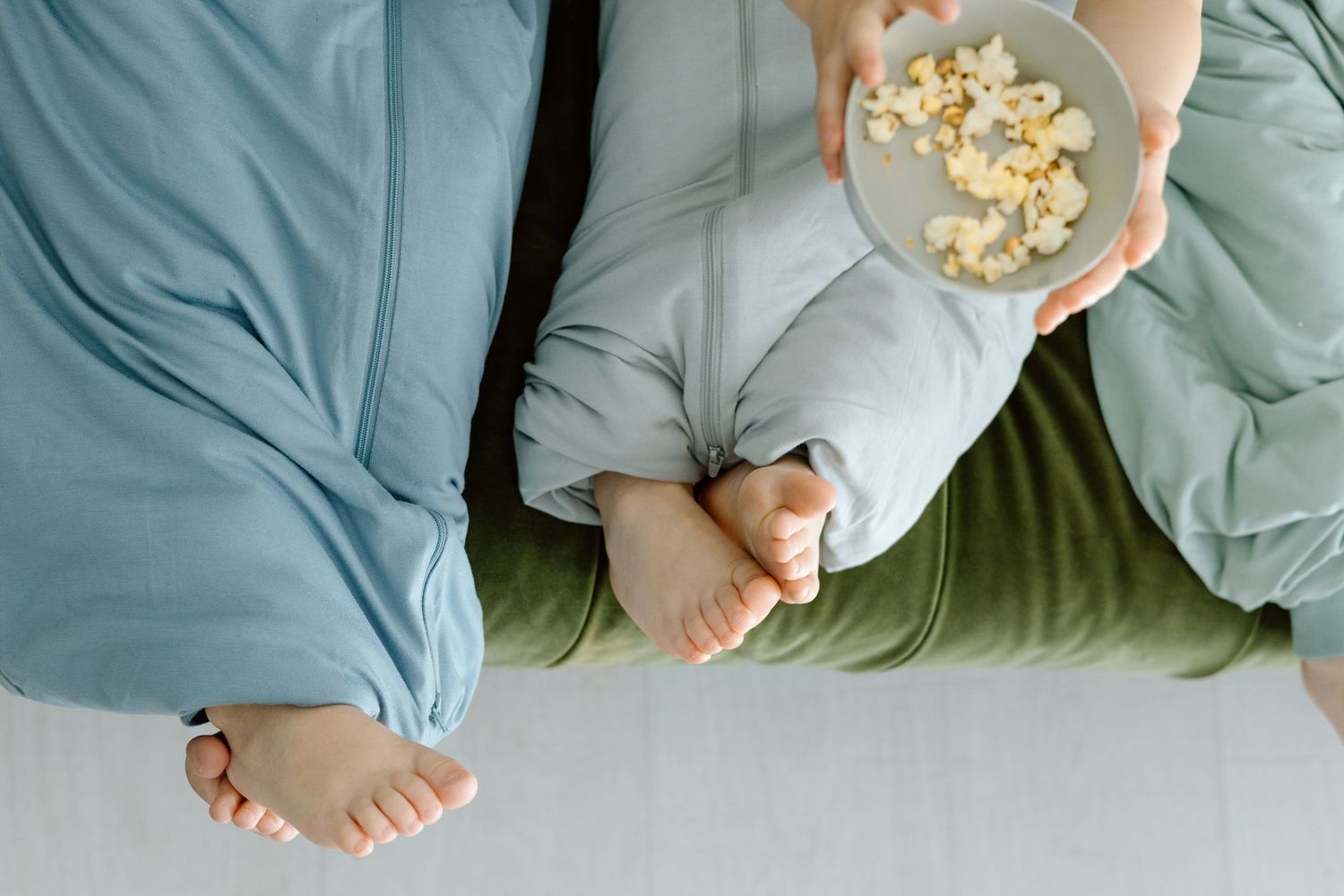 Overhead view of two people in pajamas sharing bowl of popcorn while relaxing together.