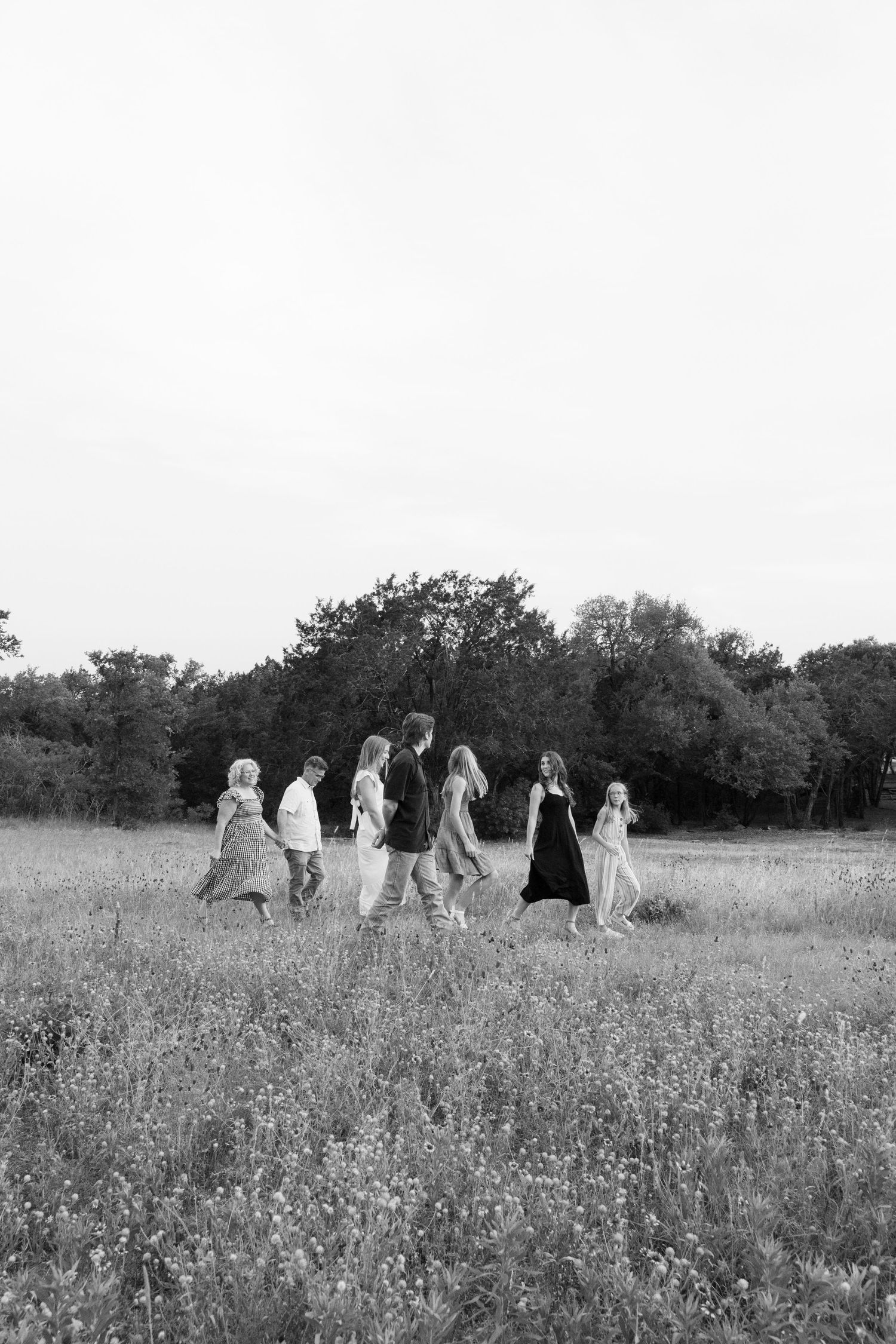 Black and white photo of a family of seven walking together through a wildflower meadow.