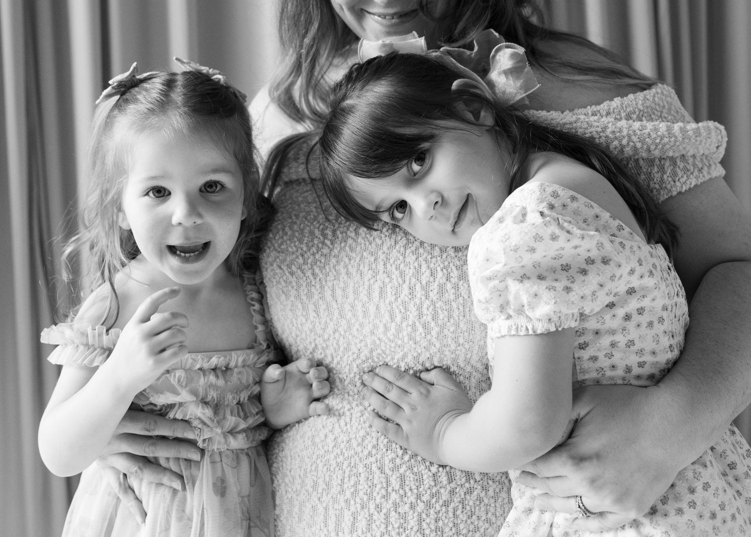 Black and white photo of a pregnant mother hugging her two young daughters during a maternity photo session.