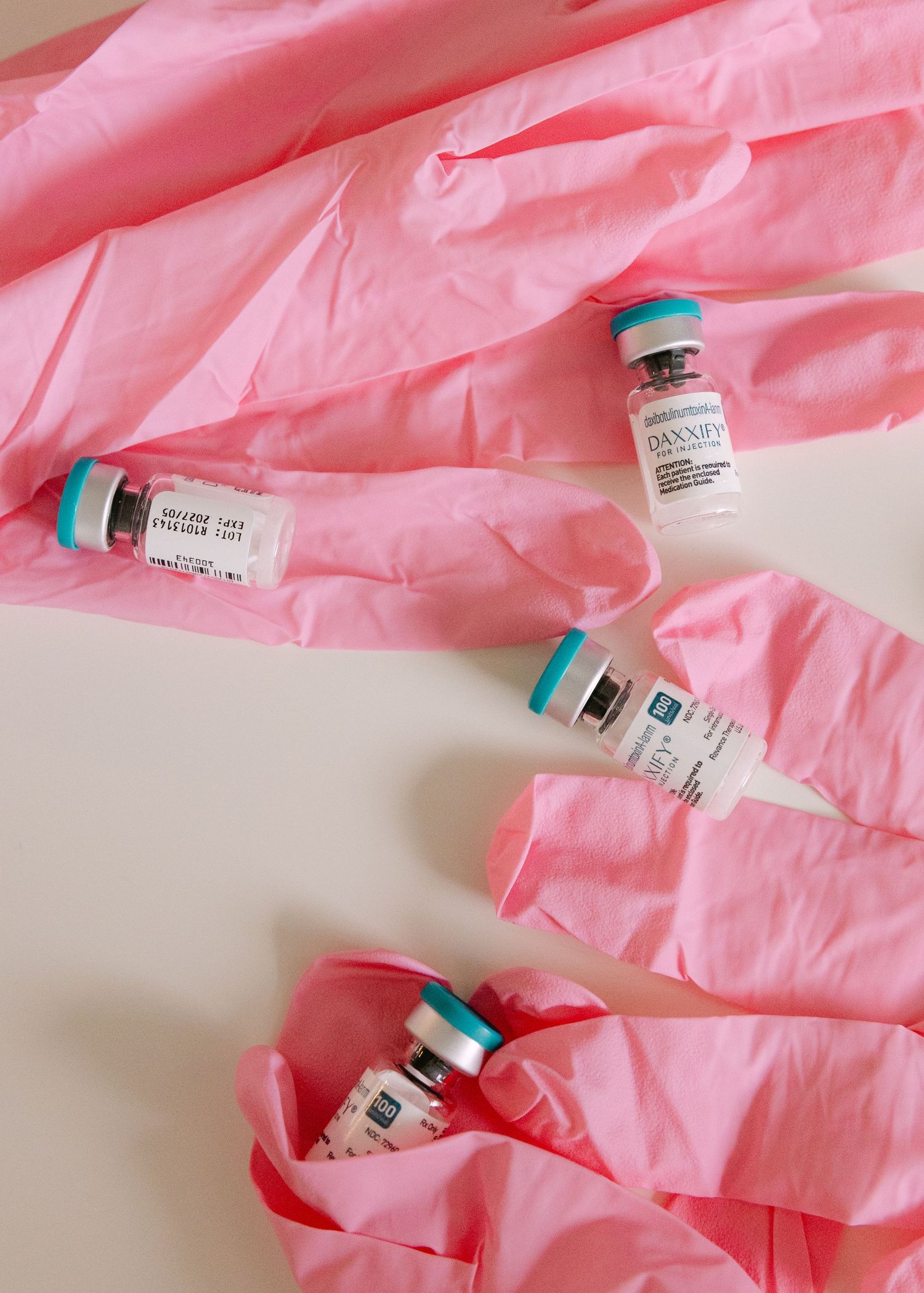 Four Daxxify neurotoxin injectable vials arranged on pink medical gloves on white surface.