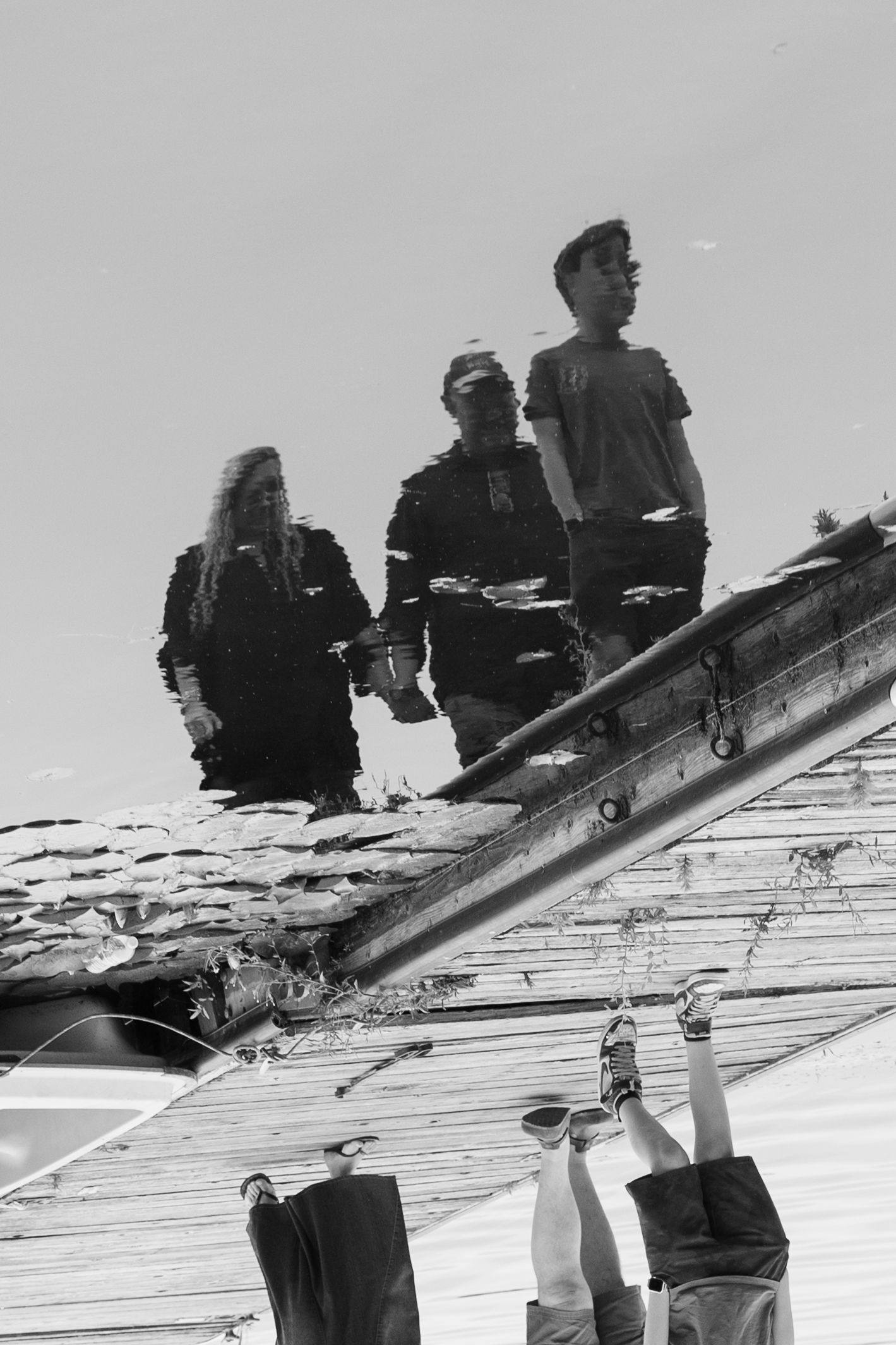 Black and white reflection photo of three teenagers standing on a rooftop captured in a puddle below.