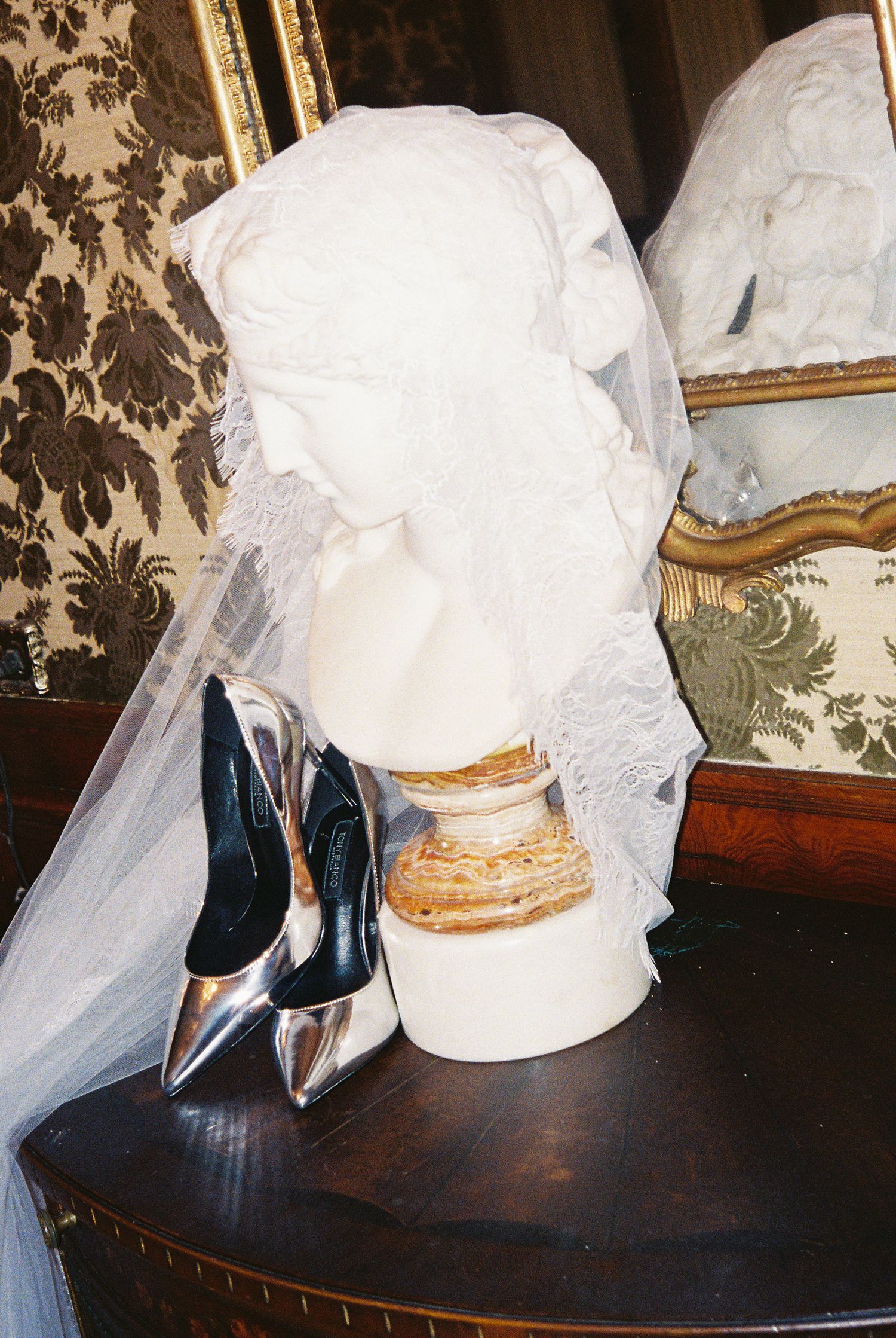 Silver metallic bridal heels beside a white lace veil on an ornate mannequin head.