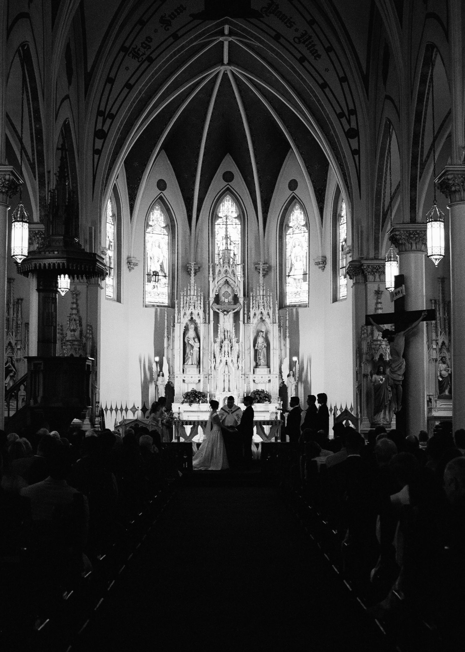 Black and white photo of wedding ceremony at Gothic cathedral altar with stained glass.