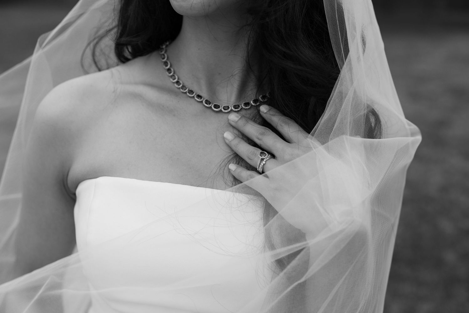 Black and white close-up of a bride in a strapless gown wearing a chain necklace and ring.