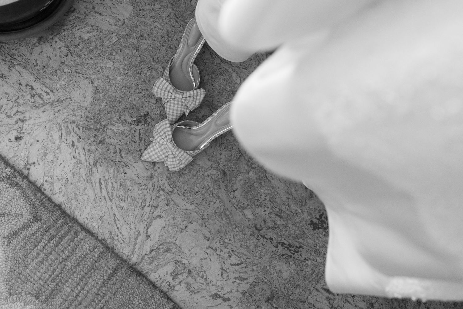 Close-up black and white photo of a bride stepping into sparkly wedding heels on a textured carpet.