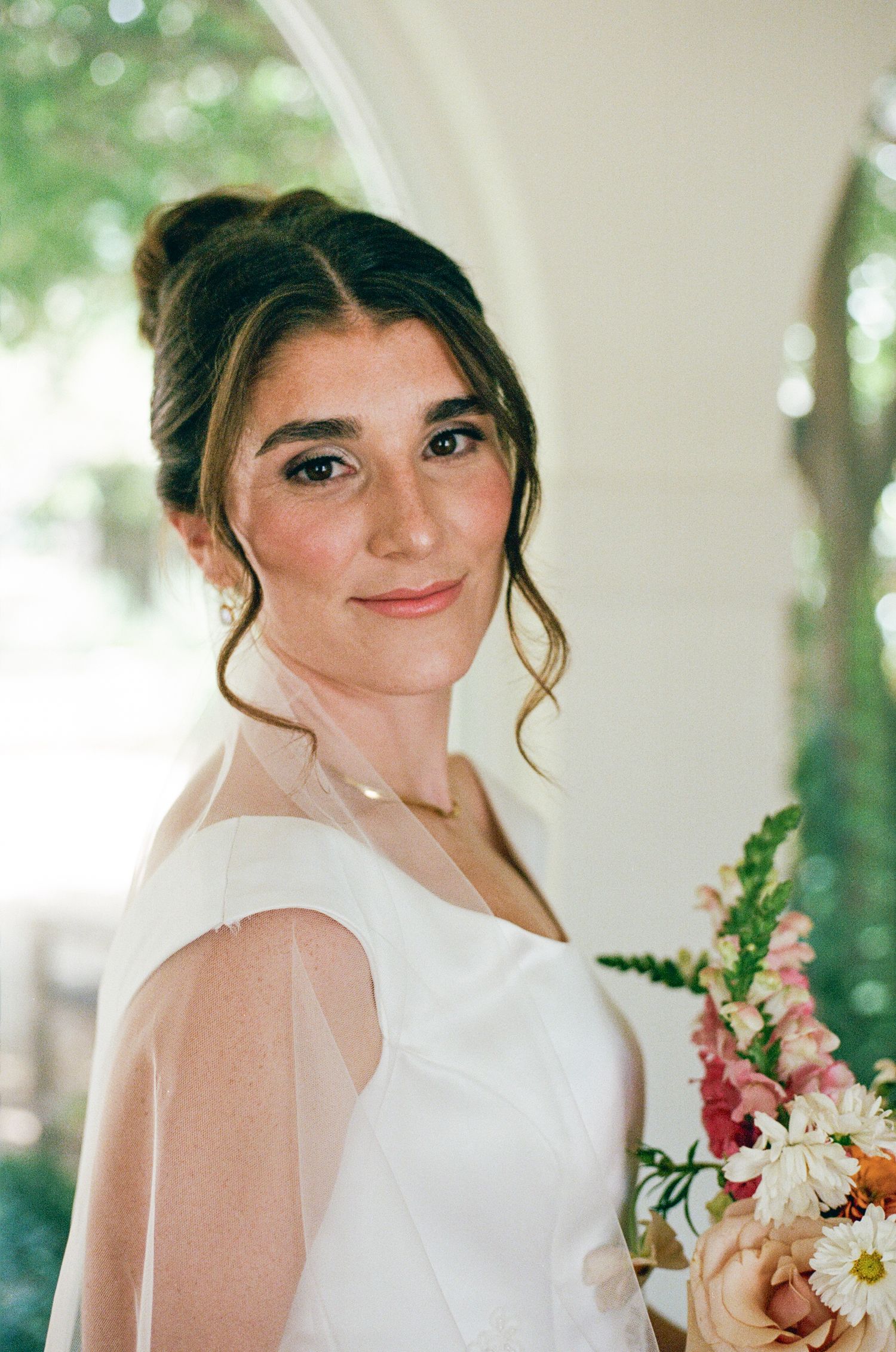 Beautiful bride with updo hairstyle holds colorful bouquet of pink and white flowers.