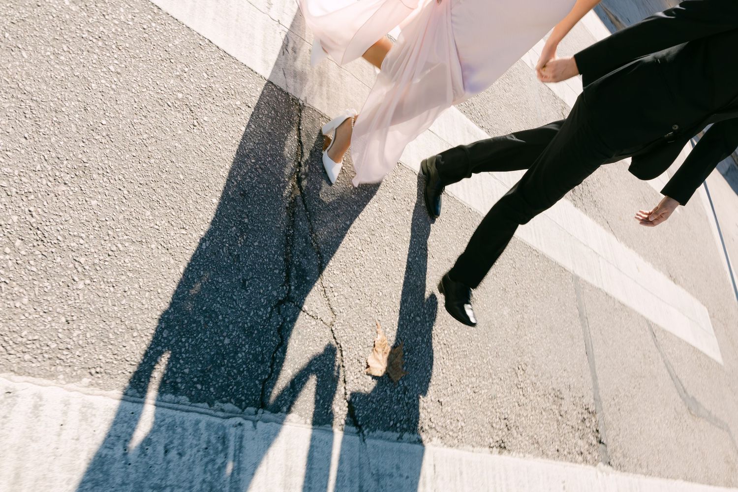 Aerial view of bride and groom casting shadows while crossing a sunny street together.
