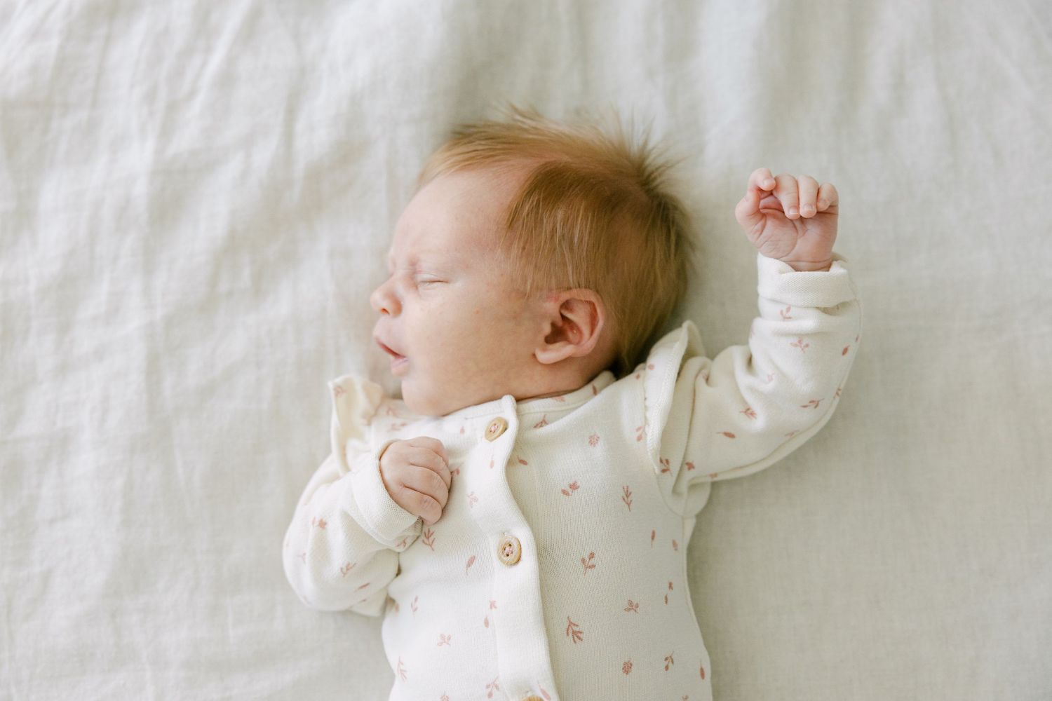 Peaceful newborn baby sleeping on white blanket with arm raised up.