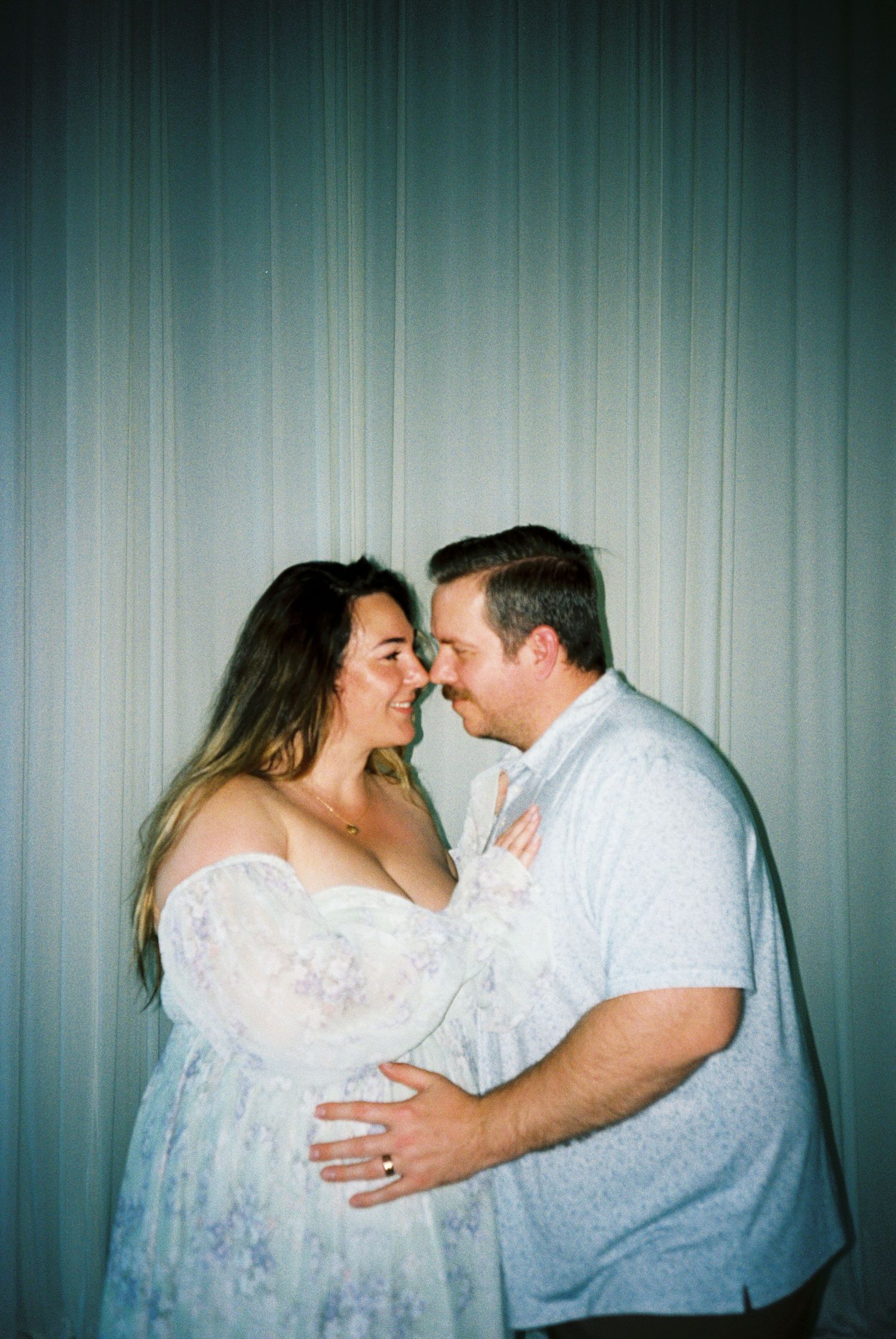 Expecting couple sharing a tender nose-to-nose moment during their maternity photo session indoors.