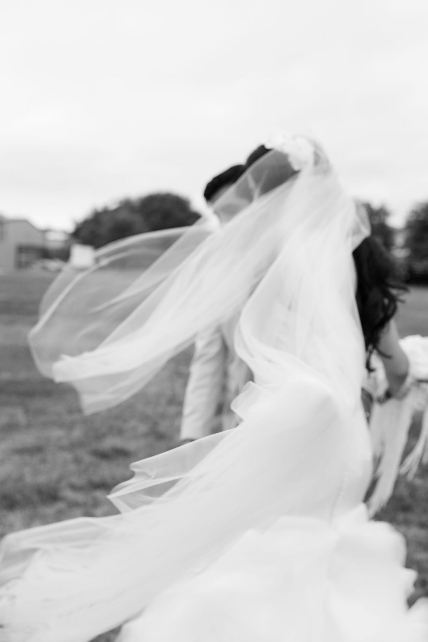Black and white artistic shot of a bride and groom kissing as her veil flows in the wind.