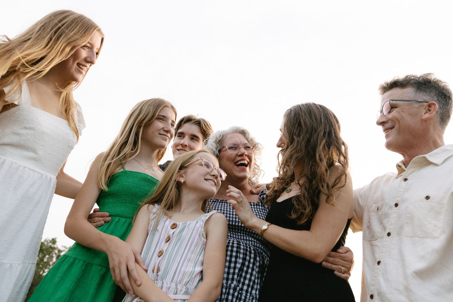 A joyful multigenerational family of seven women and girls laughing together outdoors.