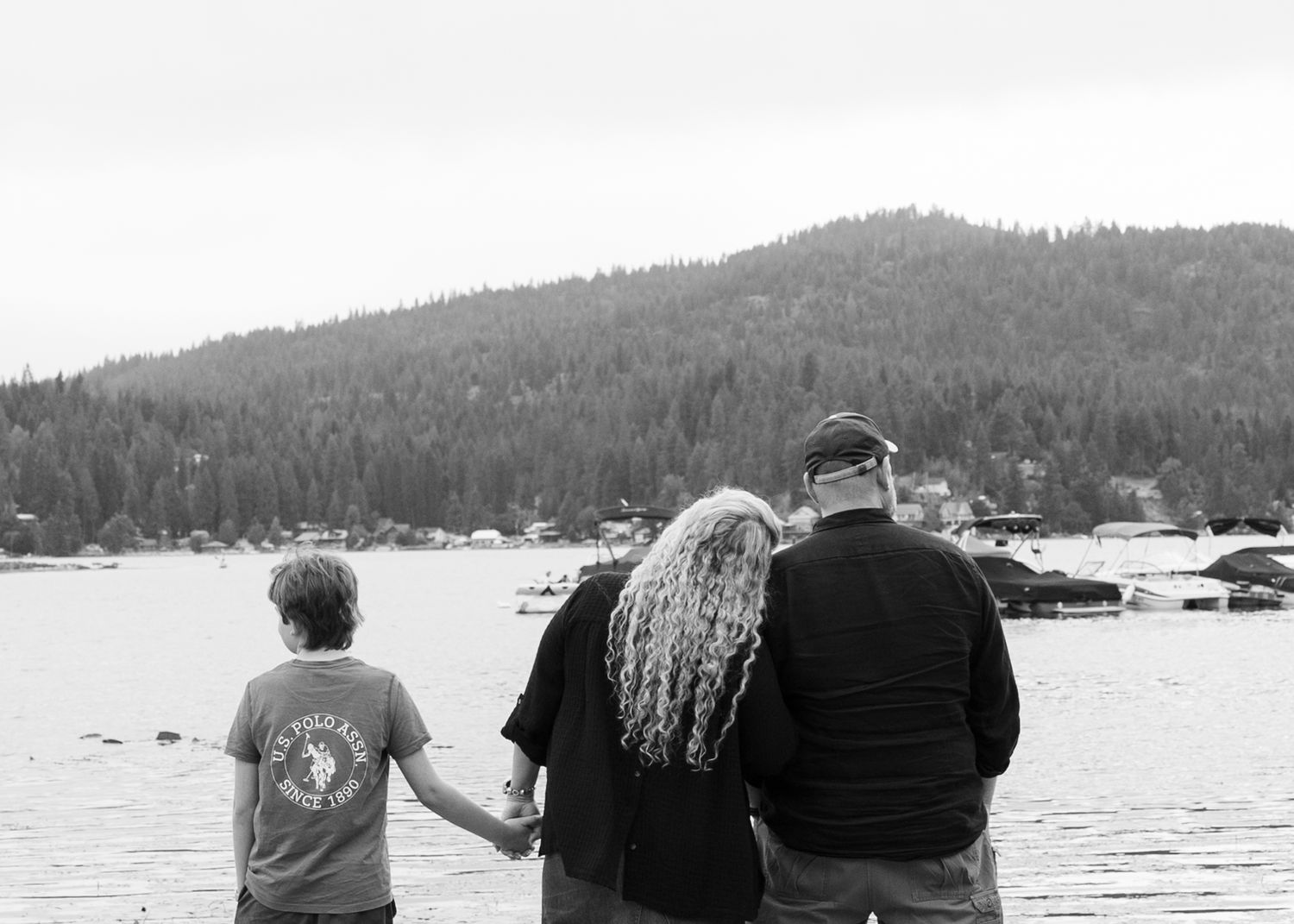 Black and white photo of grandparents and grandchild holding hands while gazing at a mountain lake landscape.