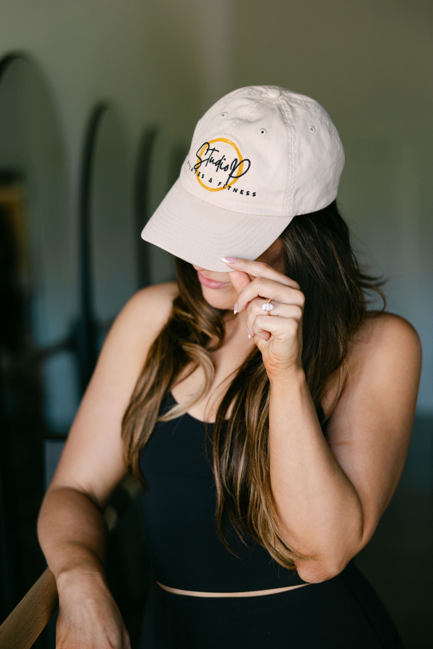 Woman wearing beige baseball cap with logo, black crop top, posing indoors.
