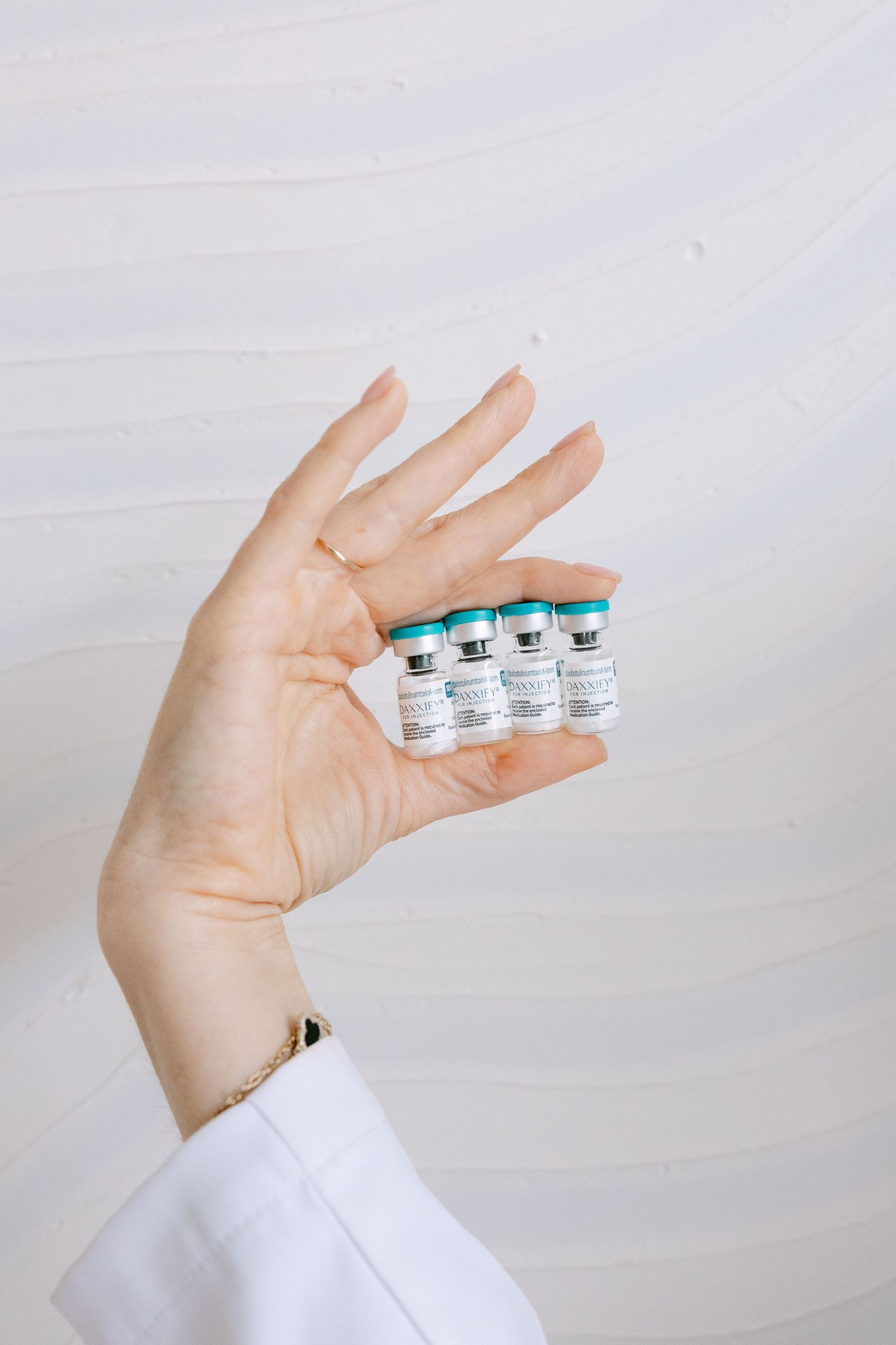 Medical professional in white coat holding four small Botox vials between fingers.