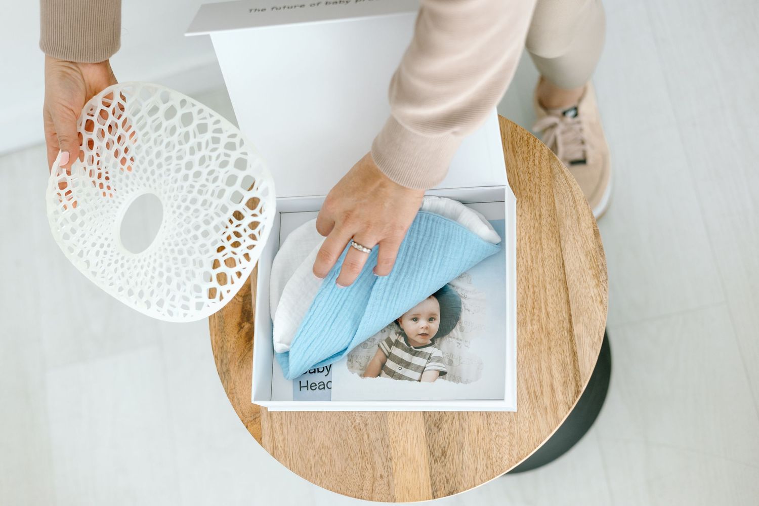Woman placing light blue baby shoes on photo book beside decorative white bowl on wooden table.