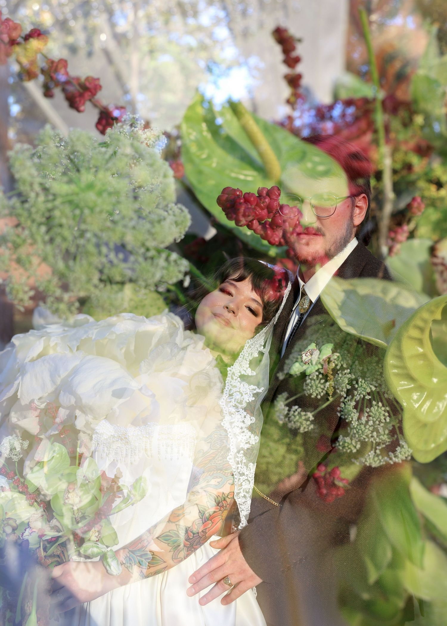 Double exposure wedding photo of bride and groom surrounded by lush green tropical leaves and red berries.