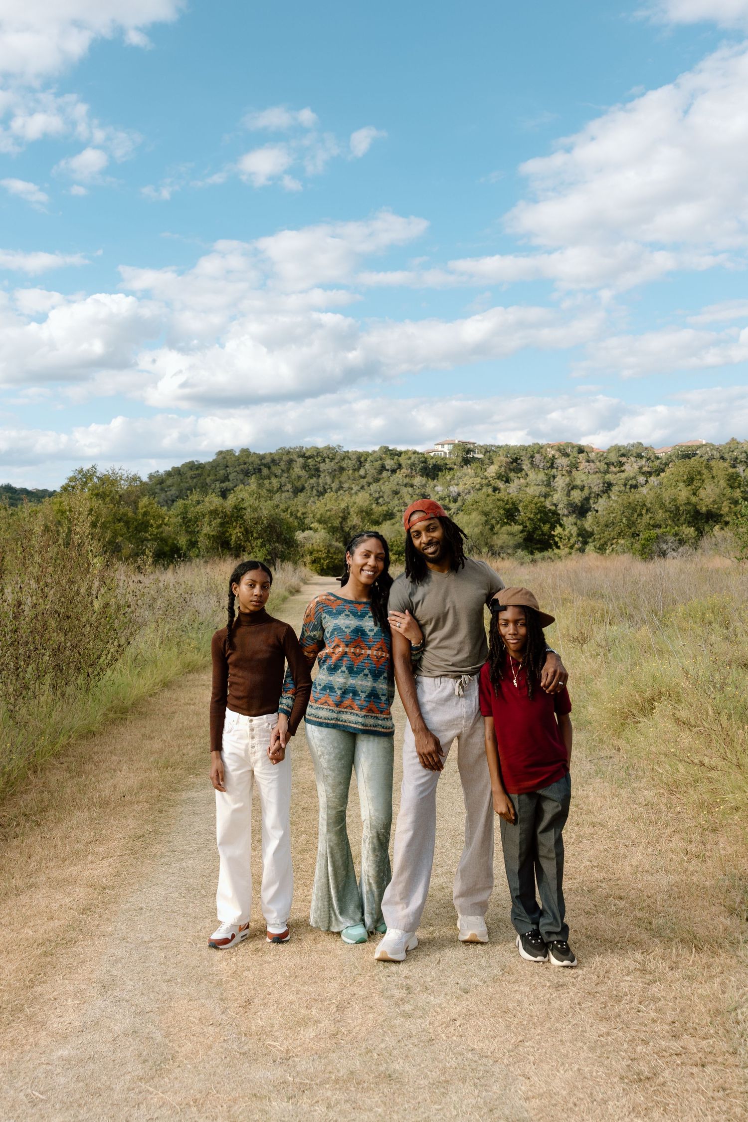 Happy family of four posing on a dirt trail surrounded by green hills.