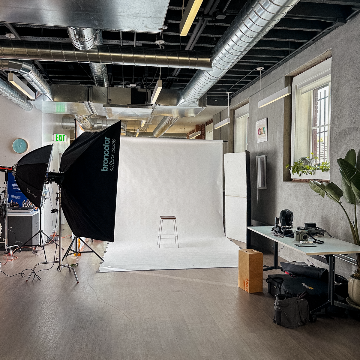 Professional photo studio with white backdrop, softbox lighting, stool, and camera equipment on wooden floor.
