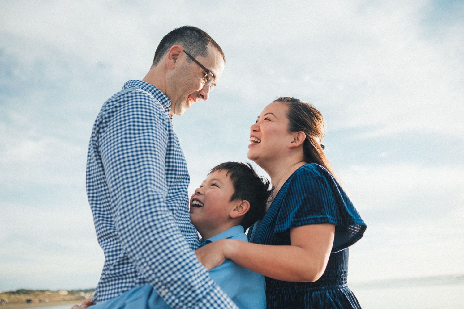 A couple embraces and laughs together against a bright blue sky backdrop.