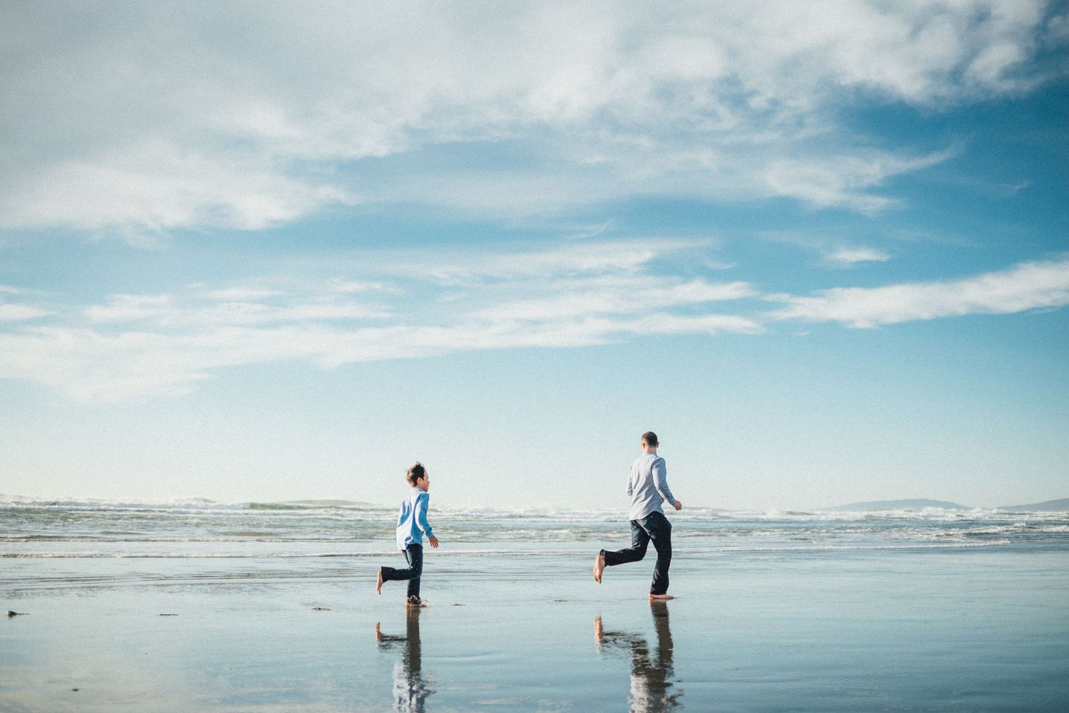 Father and son running by the water on Ocean Beach with clear blue sky at sunset. San Francisco family photography.