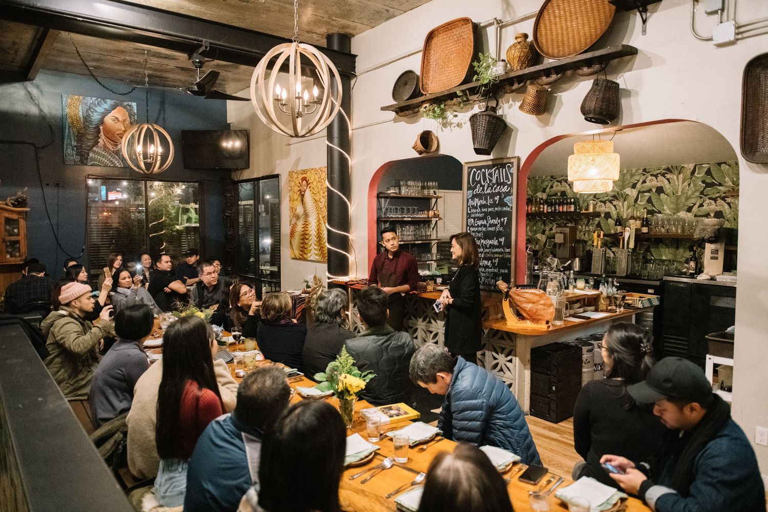 Cozy restaurant interior with diners seated at wooden tables under pendant lights and vintage decor on walls.