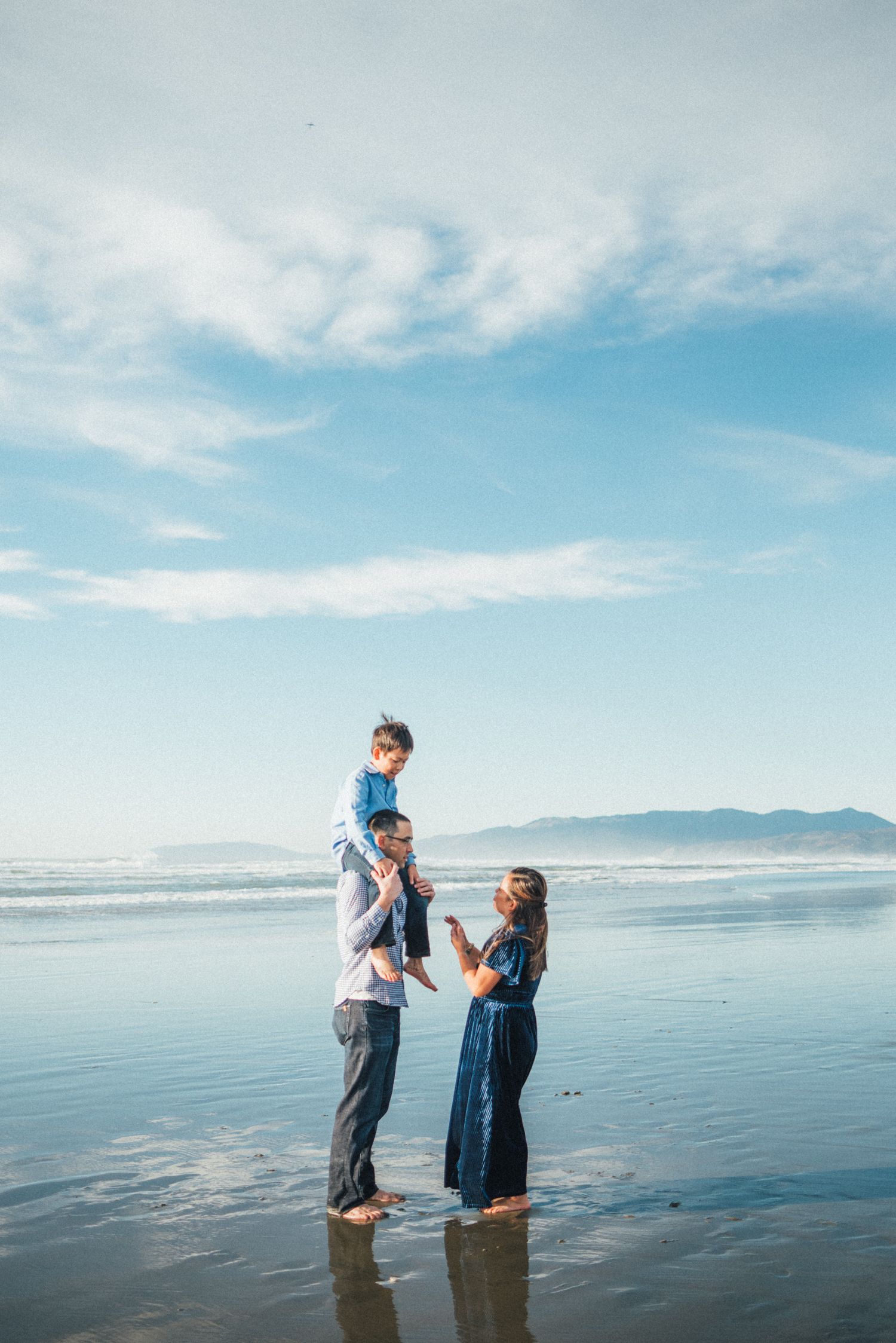 A couple stands together in shallow water at the beach during golden hour.