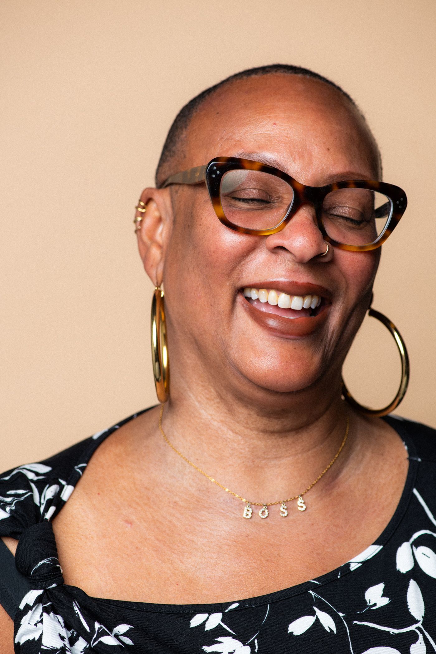 Close-up portrait wearing black and white patterned top and glasses against beige background.