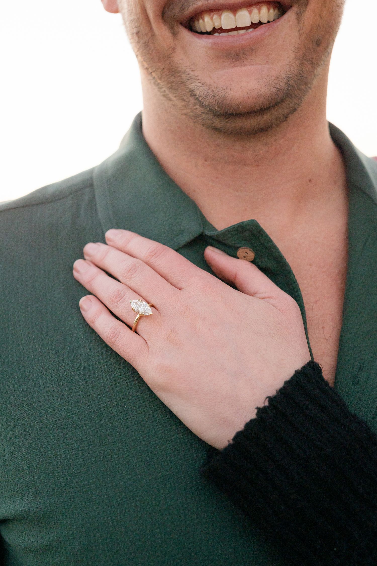 Close-up of hands showing off a new engagement ring against a green shirt.
