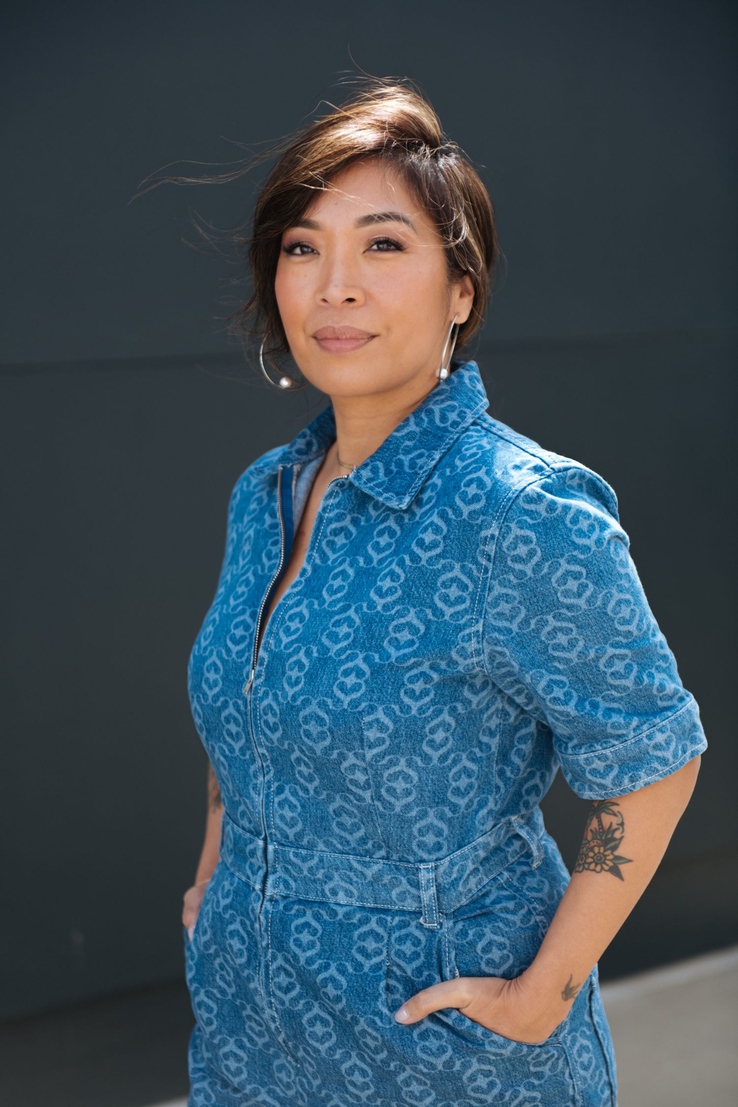Person wearing blue patterned shirt posing against dark background with visible tattoo.