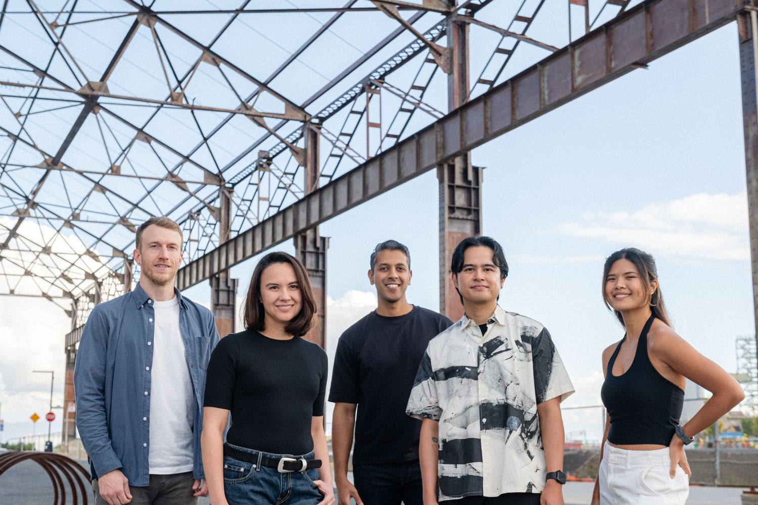 Business team poses outdoors against industrial metal structure backdrop.