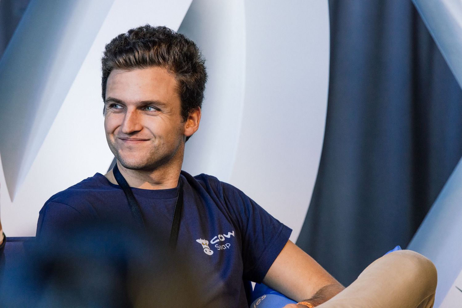 Young man in navy blue t-shirt smiling confidently while seated against a modern geometric background.