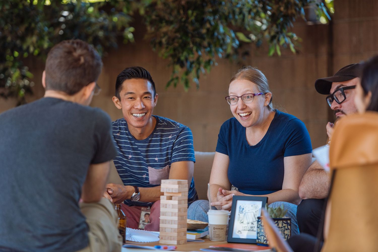 Group of friends laughing and playing Jenga together at an outdoor table, enjoying a fun social gathering.