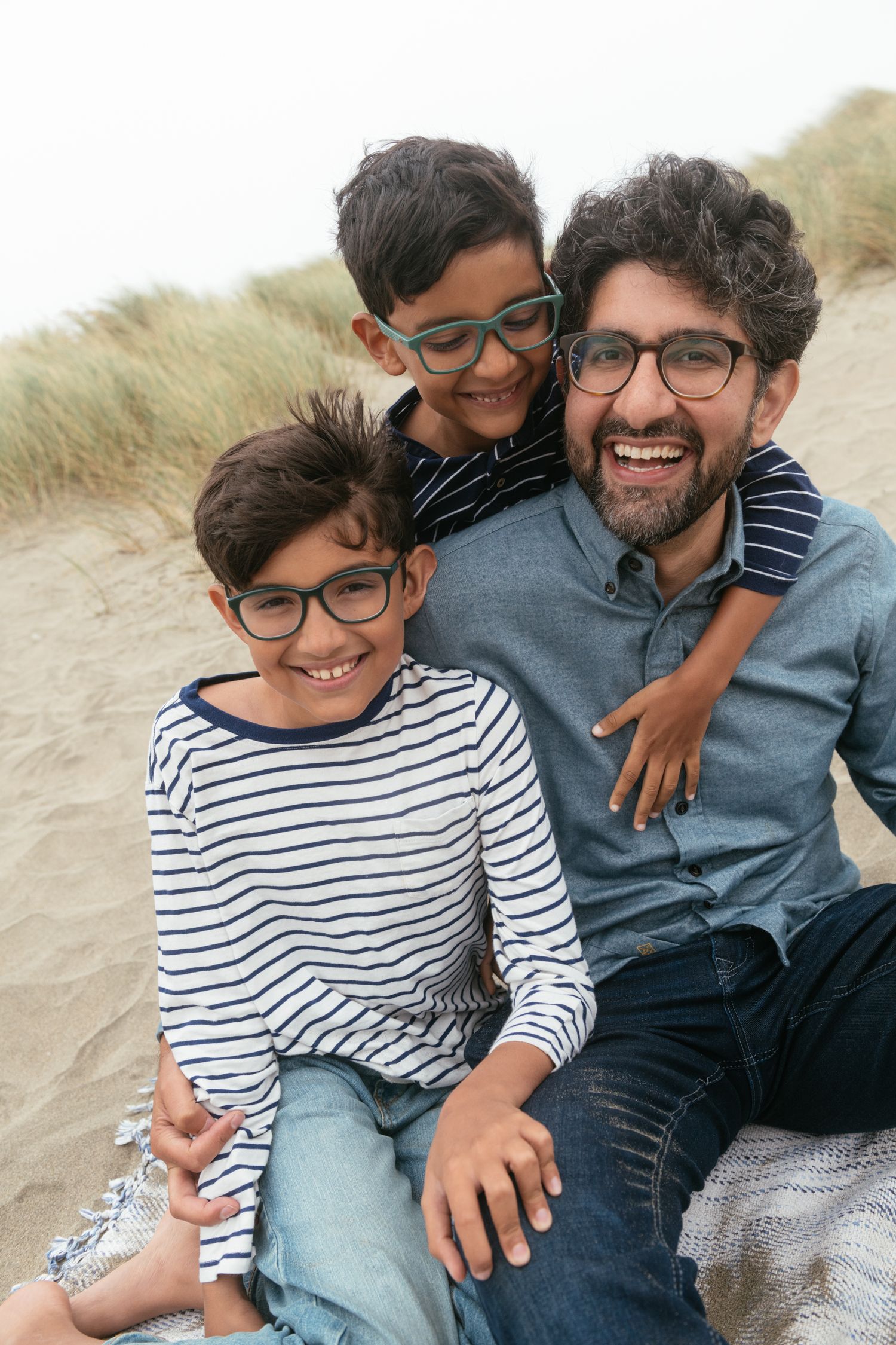 Candid beach portraits showing joyful laughter and embraces on sandy dunes.