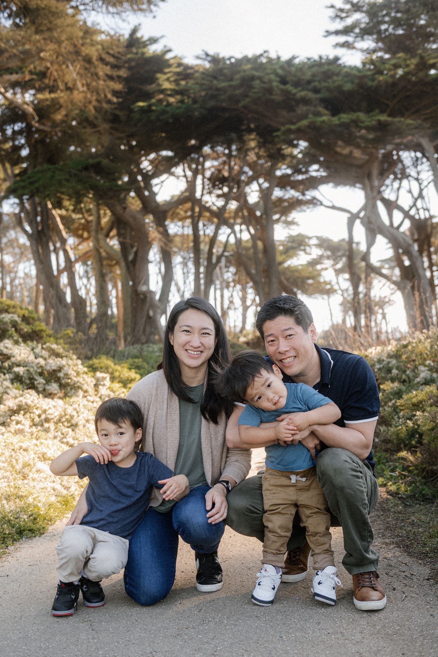 Happy Asian family of four posing on a scenic path surrounded by trees and wildflowers.