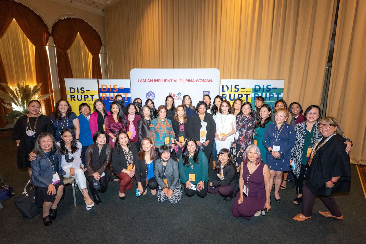 Large group of Filipino women pose together at a Disrupt conference event with motivational banners in background.