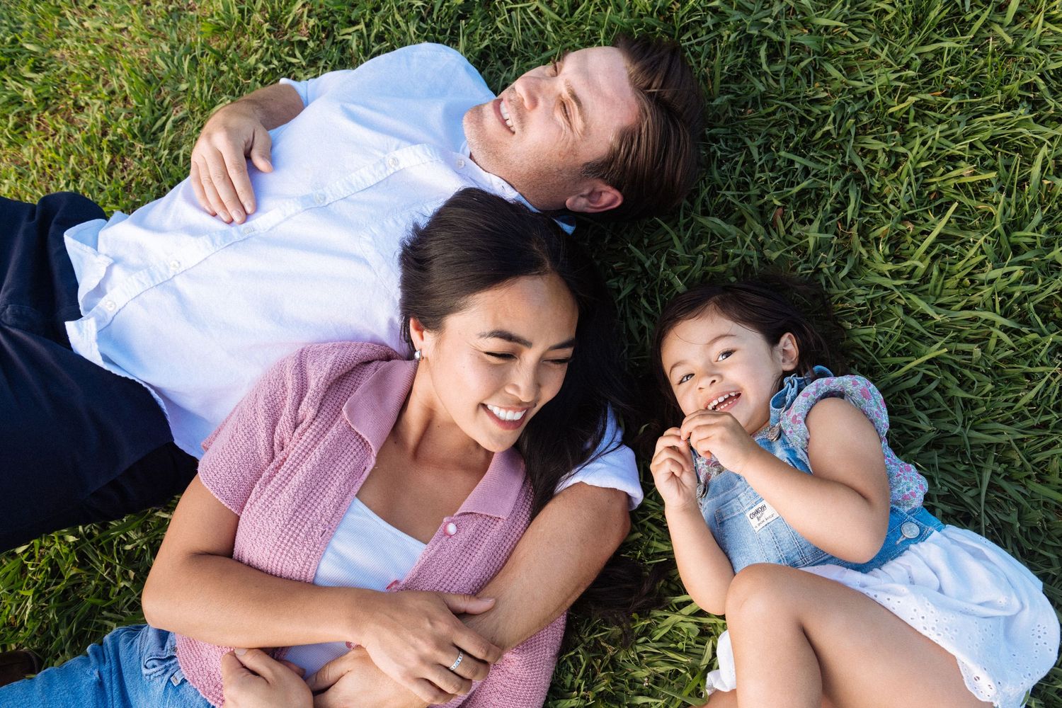 Family lying together in green grass during an outdoor photo session.