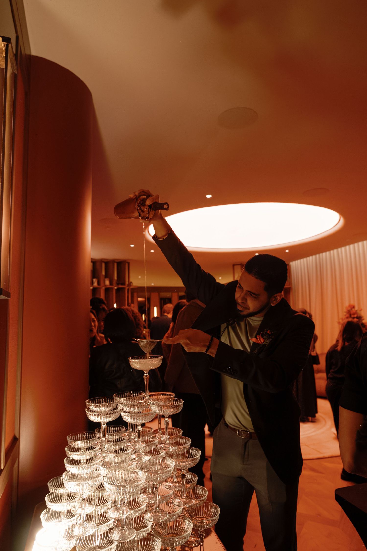 A champagne tower with stacked glasses illuminated by warm lighting at an elegant event venue.