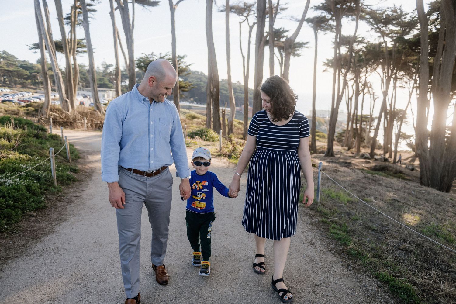 A family walks together on a tree-lined path during golden hour.