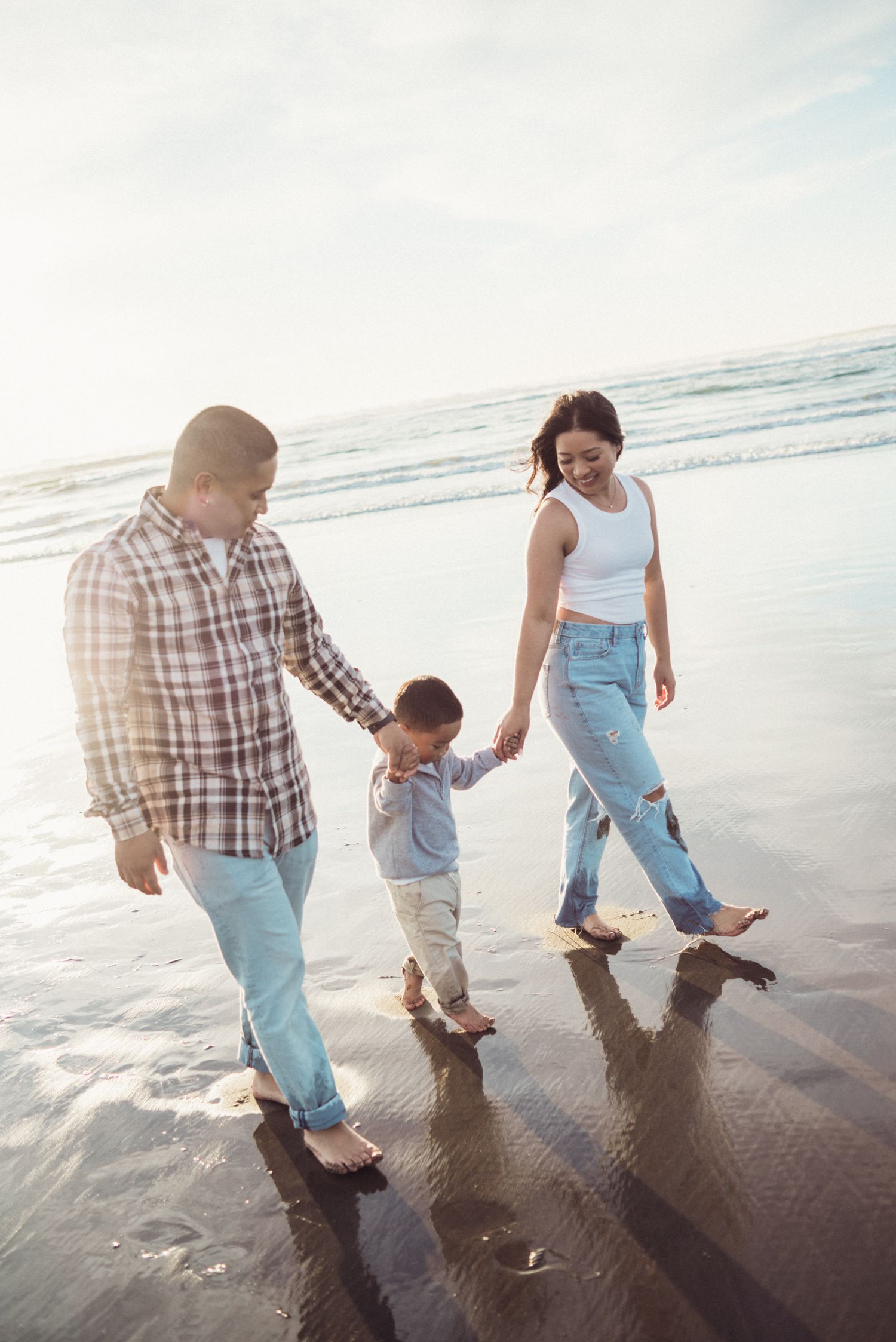 Family walking together on wet sand at the beach during golden hour.