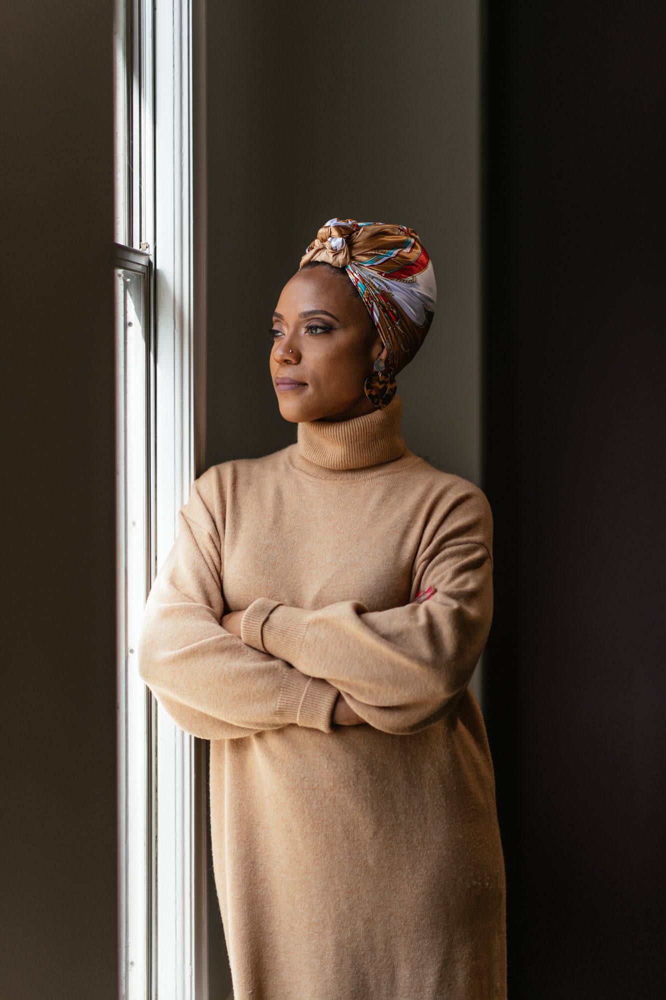 A series of moody portraits showing someone in a beige sweater and patterned headscarf looking pensively by a window.